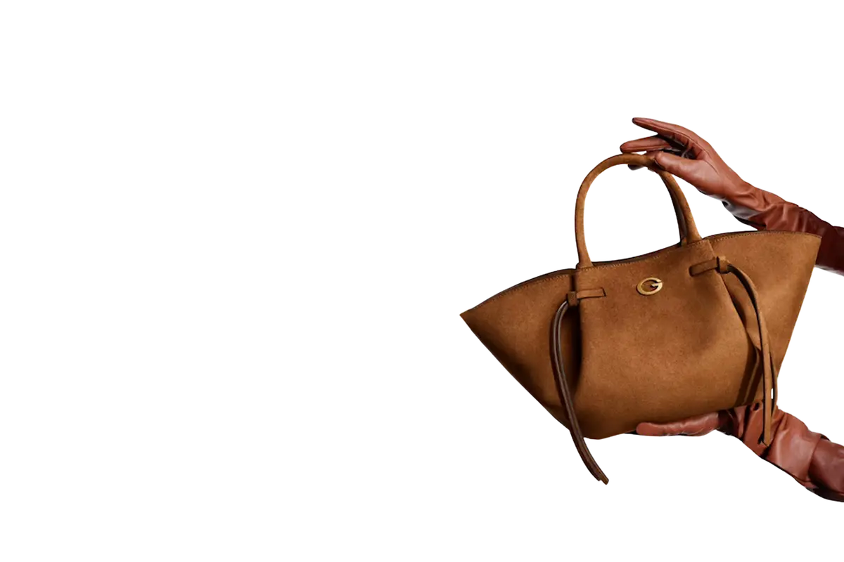 Un sac cabas Guess en daim camel, tenu par des mains gantées
